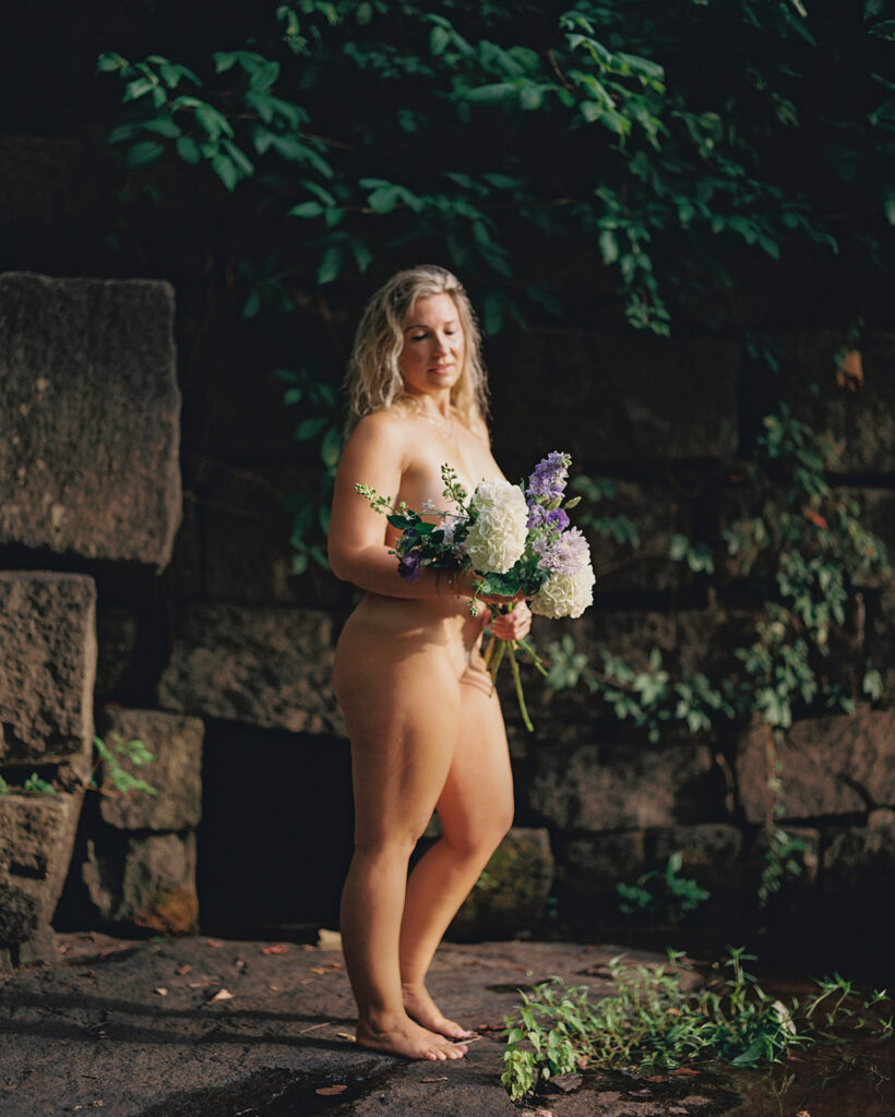 Woman with purple and white bouquet of flowers standing in golden morning light, fine art film boudoir photography by Kristen Hammock Durham NC