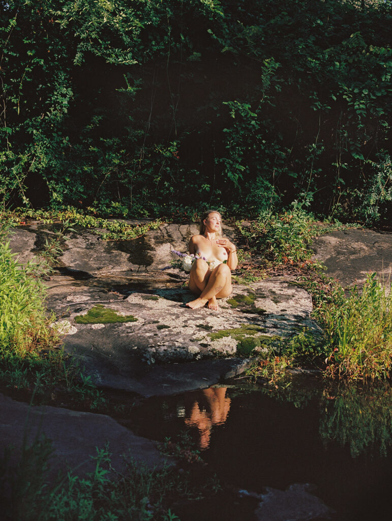 Woman sitting on lichen covered rocks in early morning light, fine art film boudoir photography by Kristen Hammock Durham NC