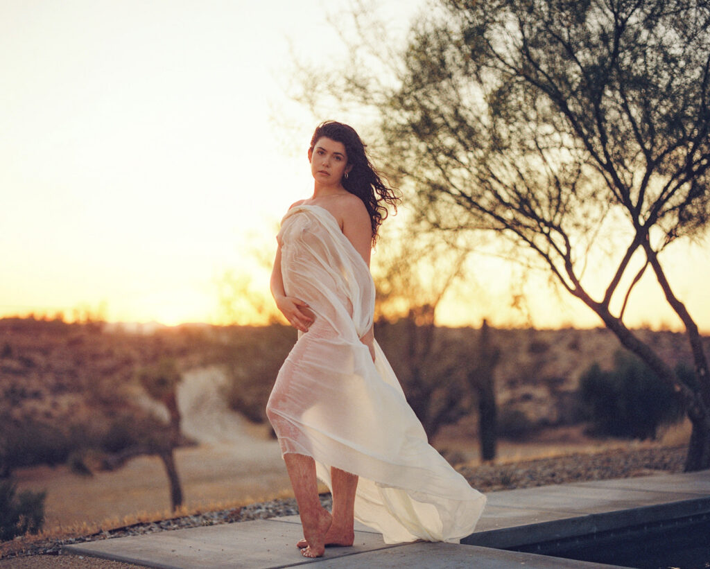 Woman wrapped in flowing white fabric at sunset during a nature-inspired fine art boudoir session.