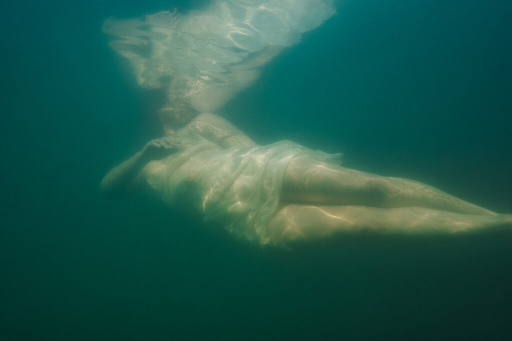 Underwater fine art boudoir portrait of a woman floating in flowing white fabric.
